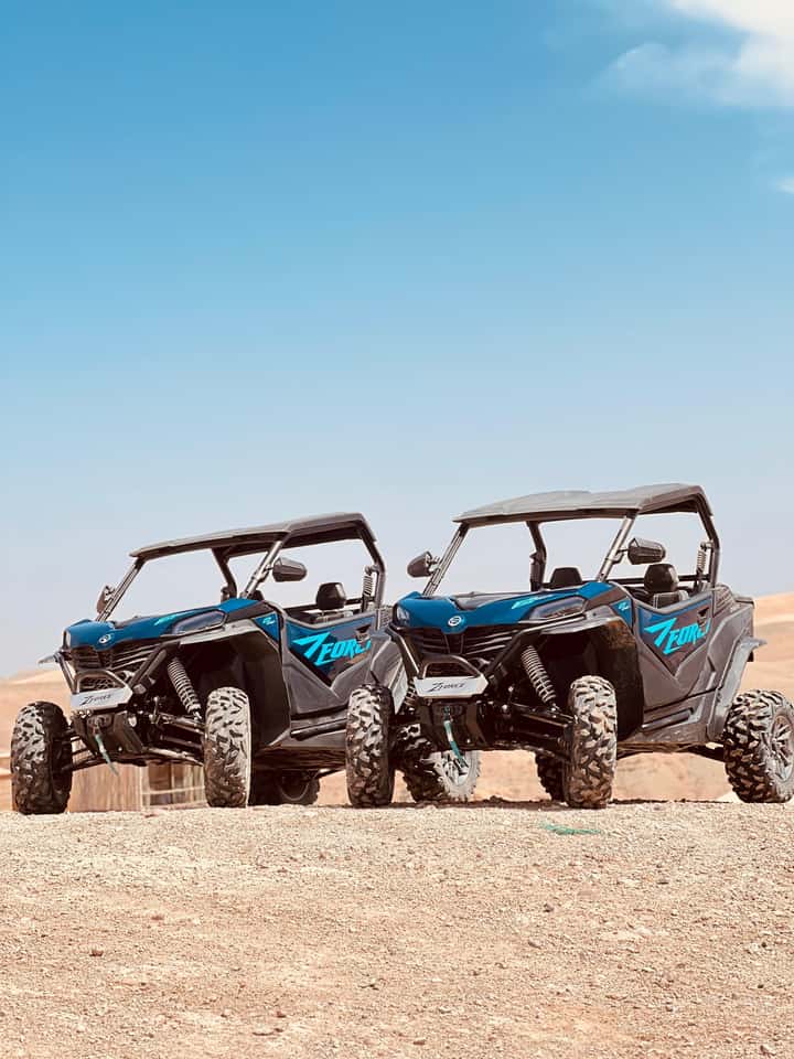 Two blue desert buggies lined up side by side on the Agafay desert plateau under a clear sky