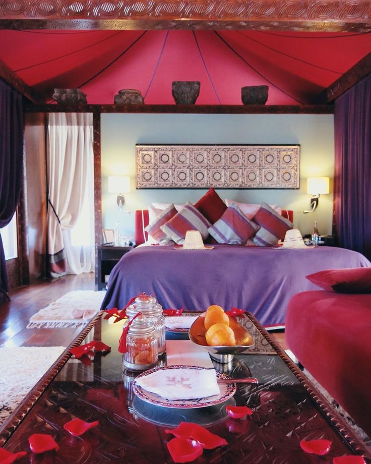 A tented suite bedroom at Kasbah Tamadot with a deep red canopy ceiling, striped cushions and a low carved table set with fruit