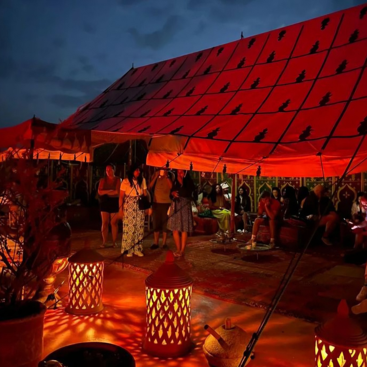 Moroccan desert dinner under a red Berber tent in Agafay, lit by lanterns after dark