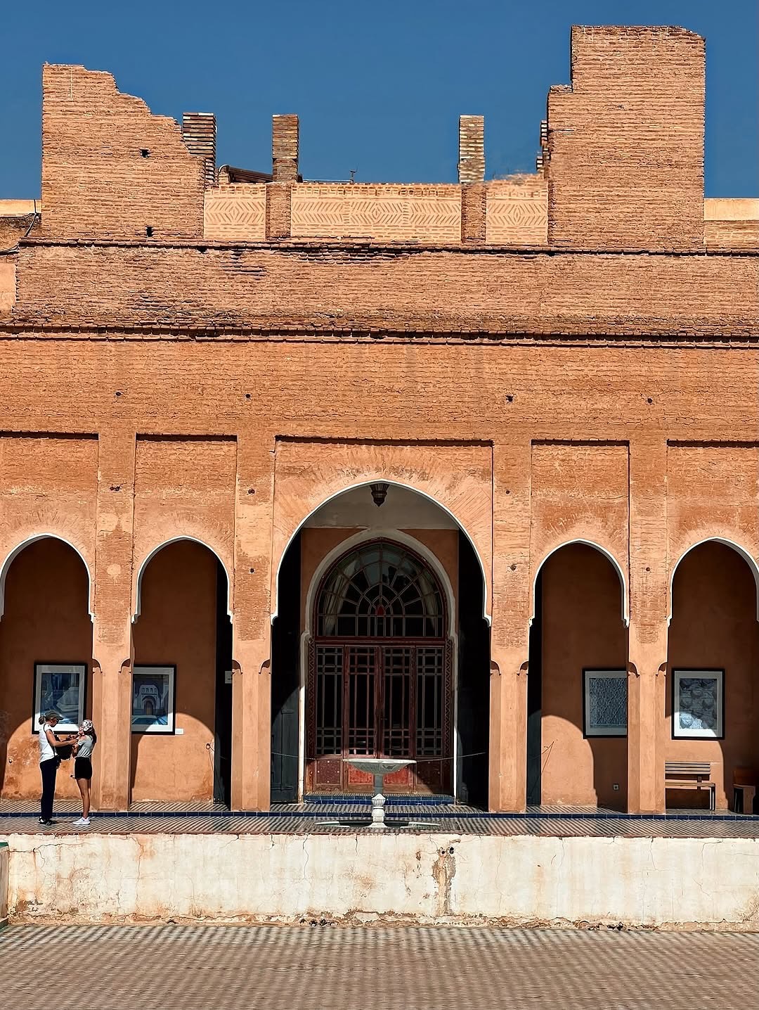 Callejón soleado en la medina de Marrakech con paredes de arcilla rosa y una puerta de madera tallada