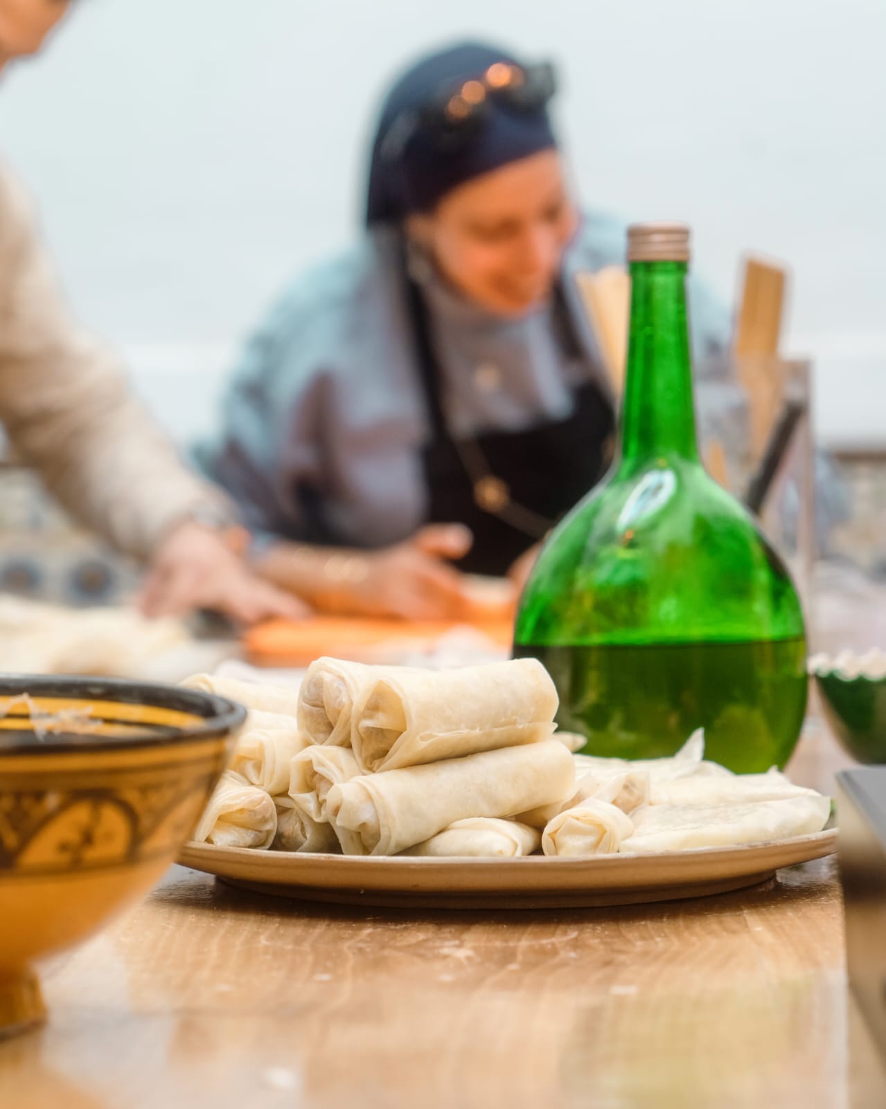 A plate of hand-rolled Moroccan pastry parcels in the foreground while a participant rolls pastry behind
