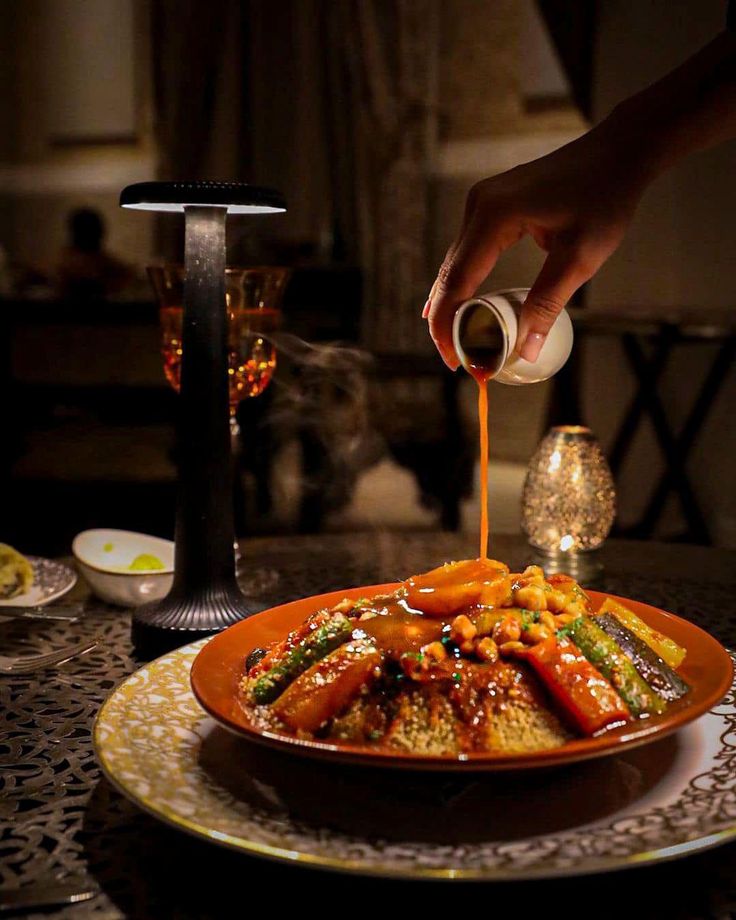Broth being poured over a couscous dish with vegetables and chickpeas at a candlelit dinner table