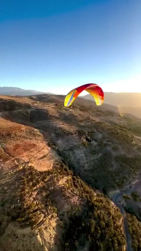 A tandem paragliding wing flying above the dry hills and valleys outside Marrakech at golden hour