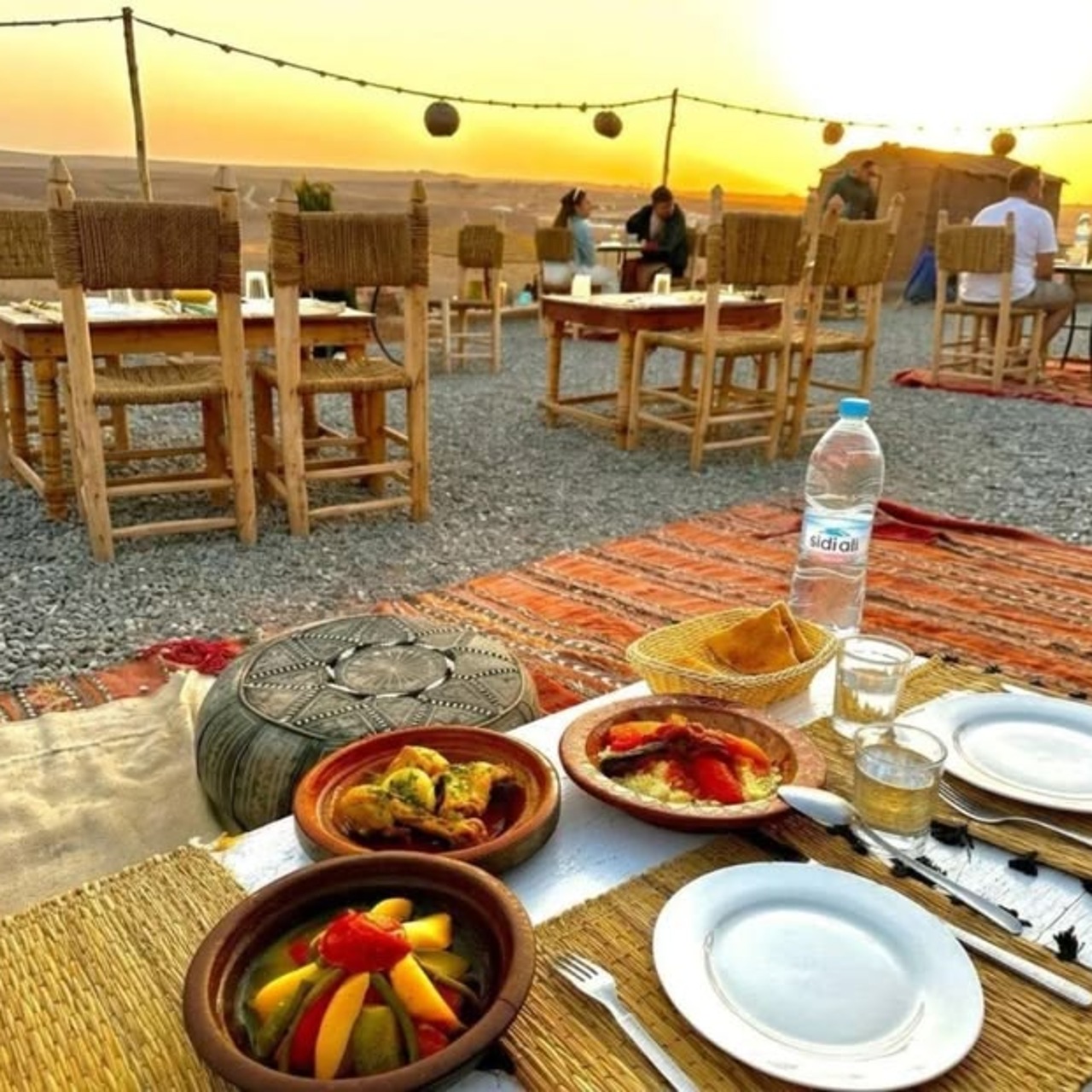 Moroccan desert dinner of tagines set on low tables in an Agafay camp at sunset