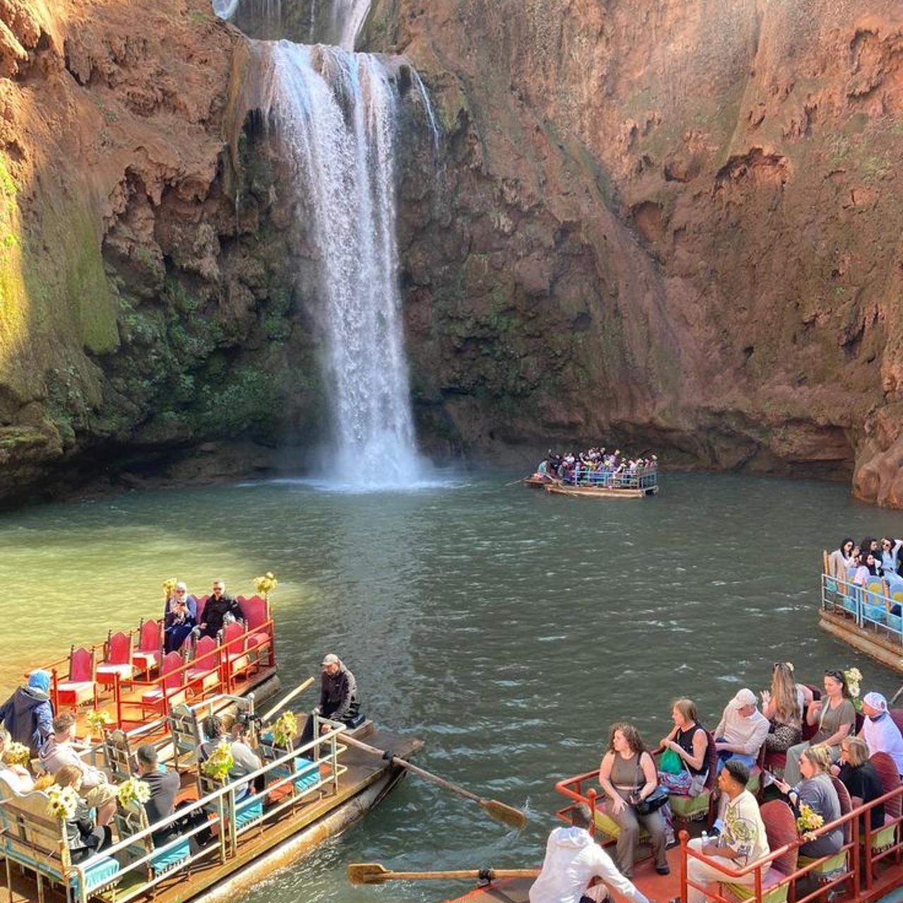 Colourful wooden boats carrying visitors on the plunge pool beneath Ouzoud waterfall