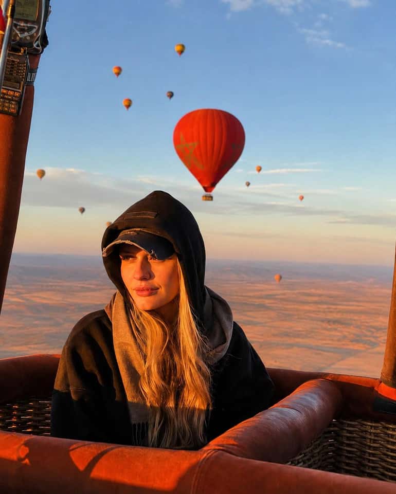 Passenger in a hooded jacket in a balloon basket with a red balloon behind her