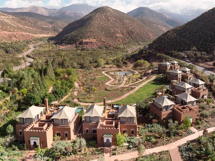 Aerial view of the pitched roofs and gardens of Kasbah Tamadot below the snow-capped peaks of the High Atlas