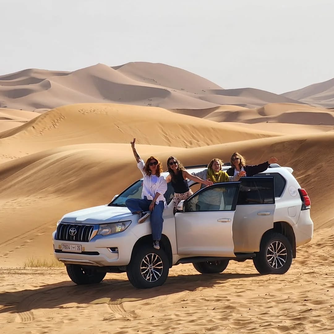 Vehículo 4x4 cruzando la carretera del desierto hacia las dunas de Erg Chebbi en un tour de Marrakech a Fez