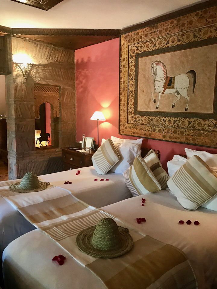 A twin room at Kasbah Tamadot with two beds dressed in white linen, straw sun hats, rose petals and a framed painting of a horse