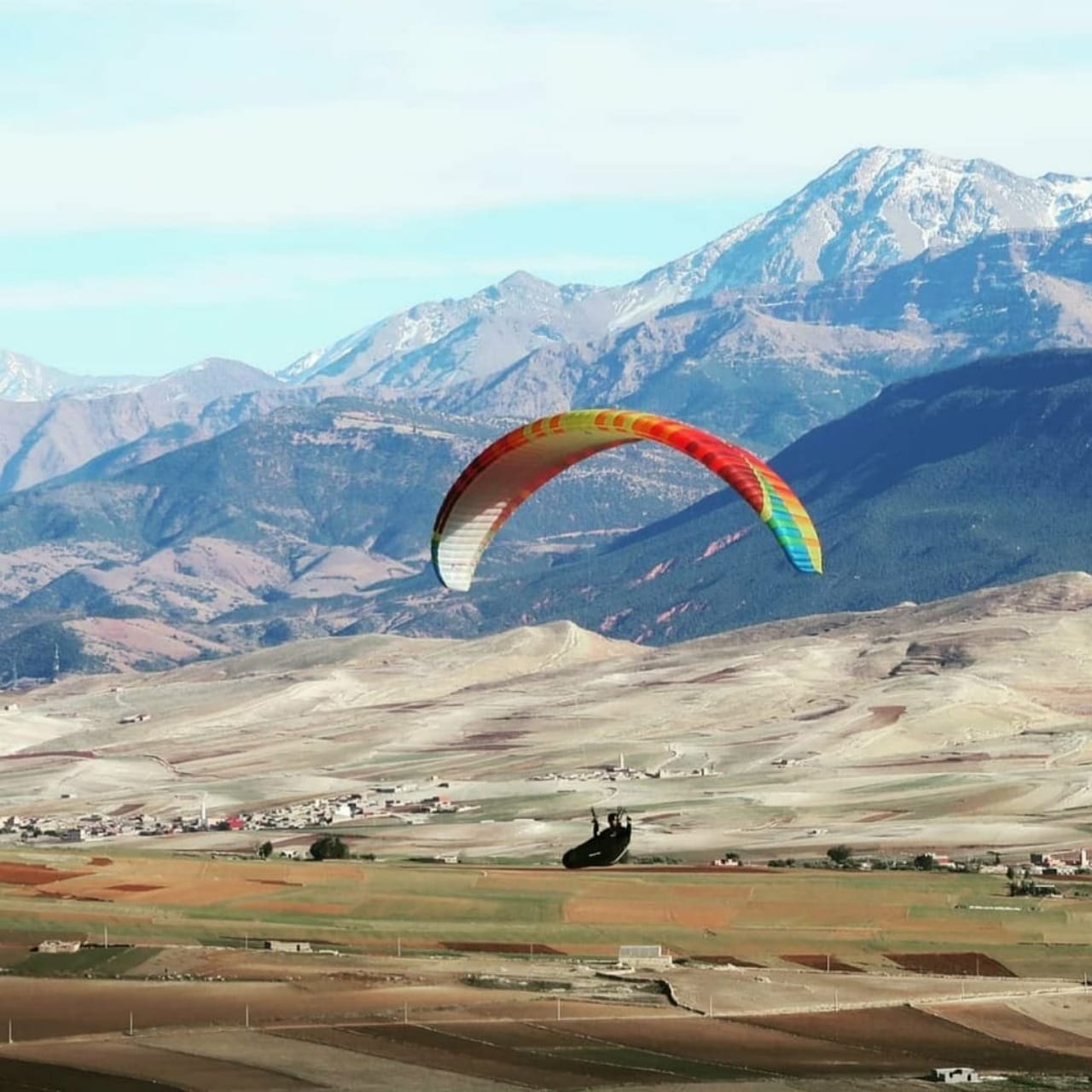 Colourful paraglider flying with the snow-capped High Atlas mountains behind