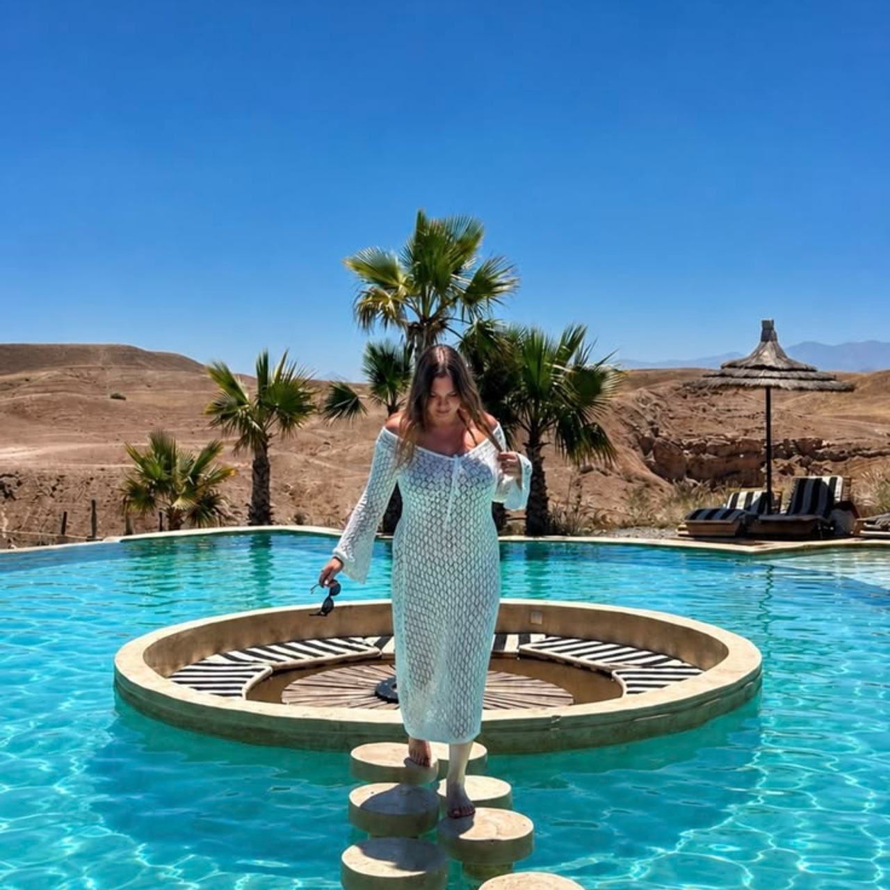 A guest by a desert pool framed by palms with the Agafay hills behind
