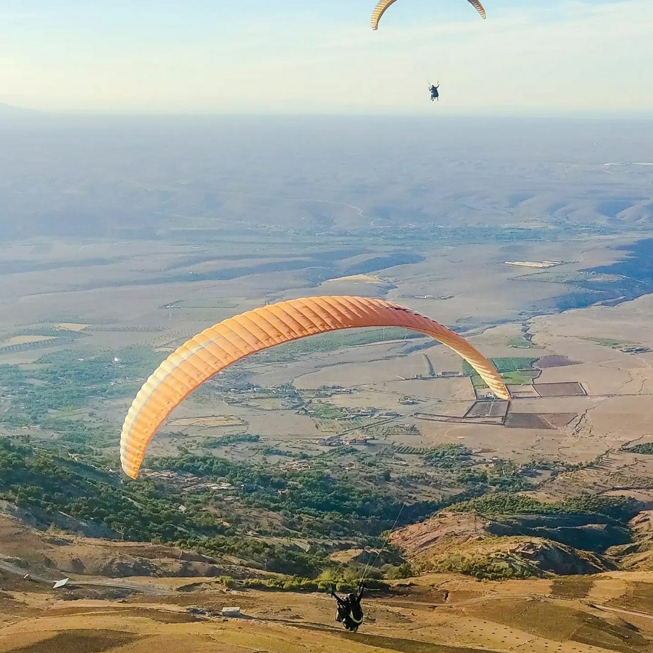 Paraglider high above the Haouz plain and Atlas foothills with a second wing beyond