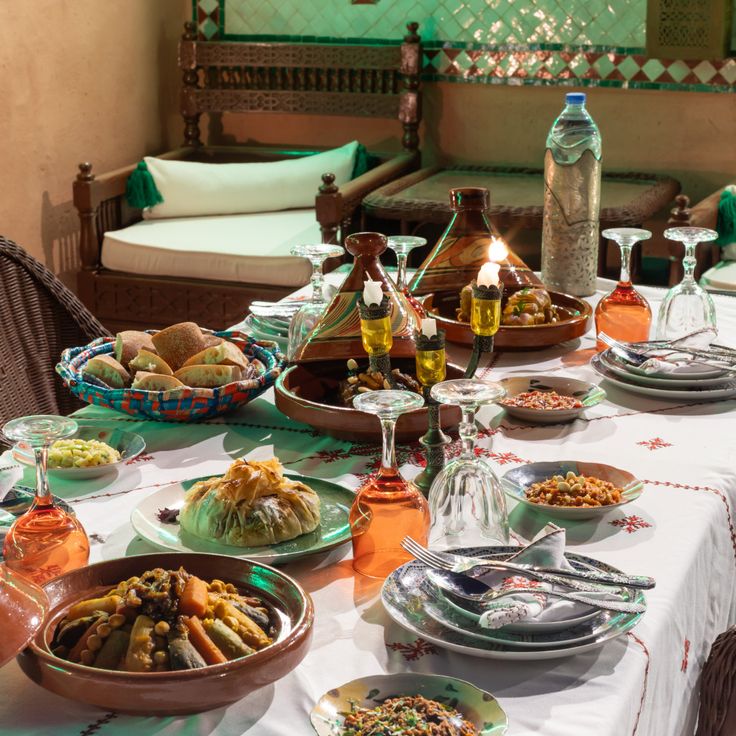 A riad dinner table set with tagines, salads, bread and glassware beside carved wooden banquettes