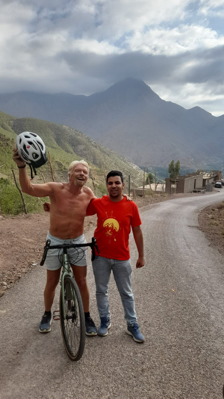 Mustapha Amazouz with a cycling guest on a mountain road in the High Atlas below the peaks