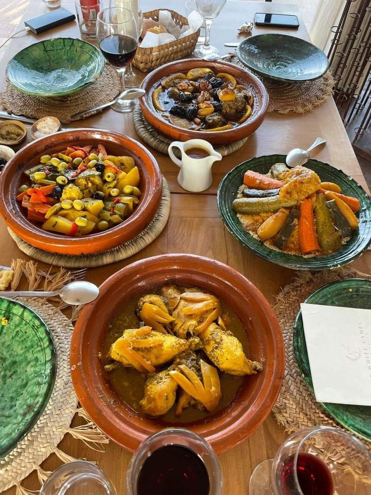 Mesa con varios tajines, cuscús con verduras, ensaladas, pan y copas de vino