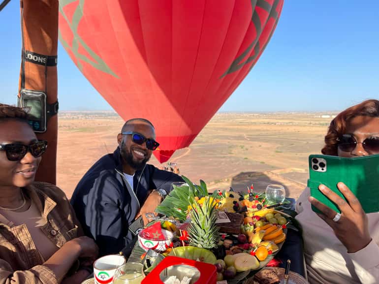 Three passengers in a balloon basket with fruit and snacks