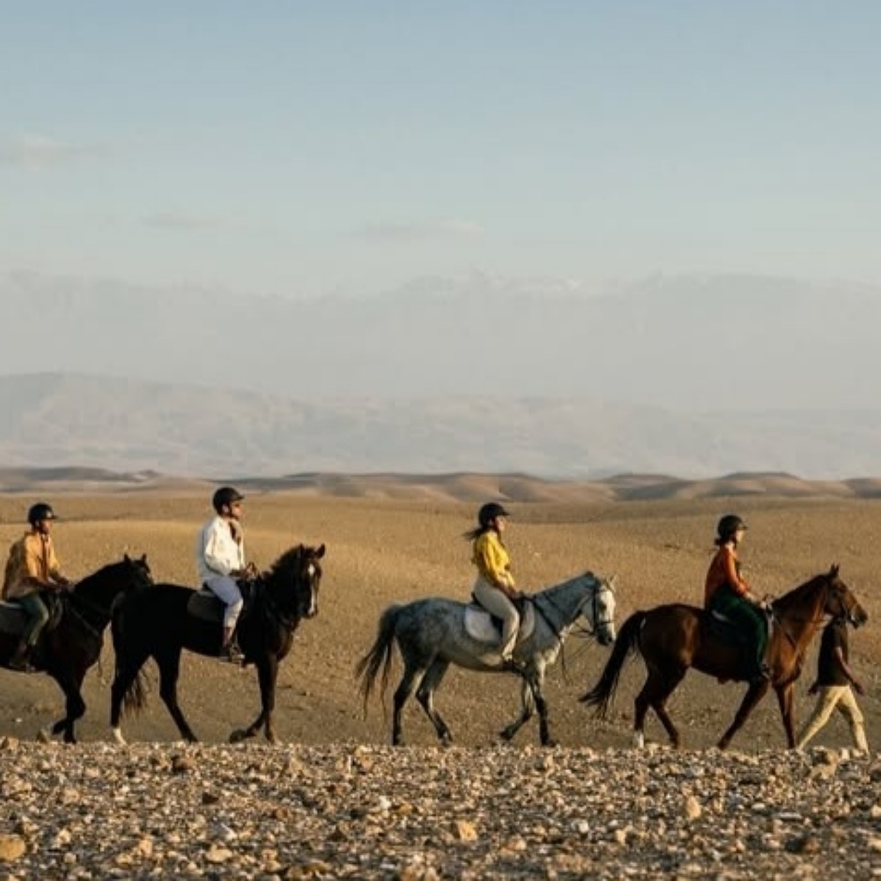 Four riders in helmets crossing the stony Agafay desert at golden hour