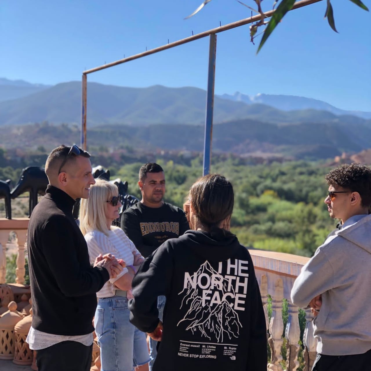A local guide briefing travellers on a terrace with the High Atlas behind them