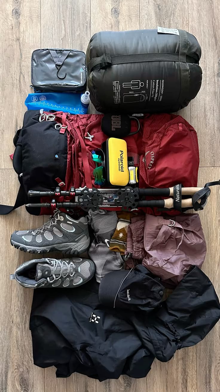 A trekker packing kit laid out: boots, trekking poles, sleeping bag, warm layers and waterproof jacket