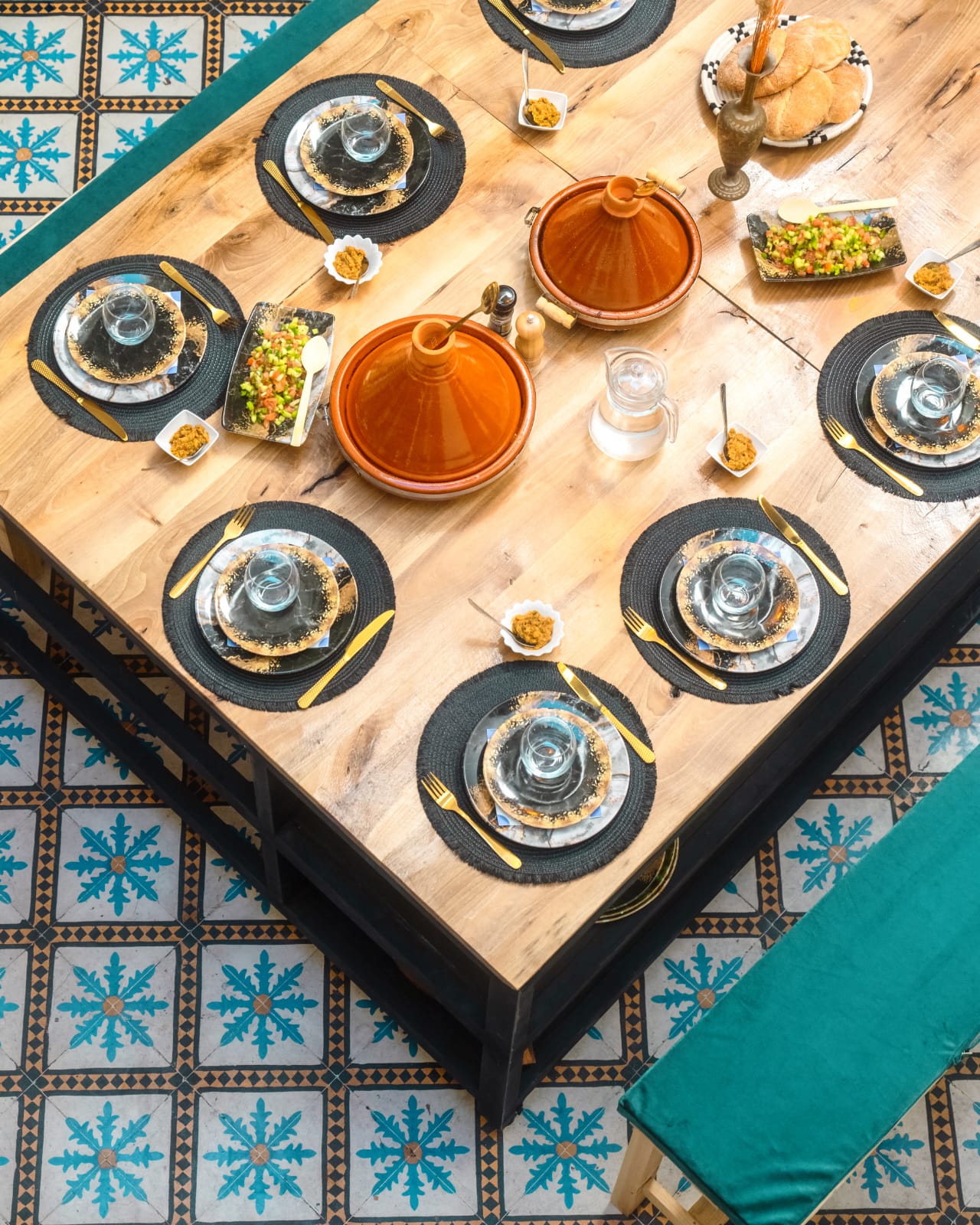 Overhead view of the riad table laid with two clay tagines, salads, bread and gold cutlery before the meal