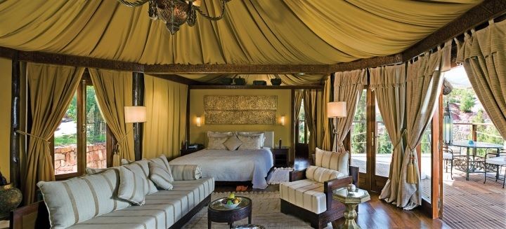 A Berber tent suite at Kasbah Tamadot with a canopied ceiling, bed, sofa and doors opening onto a terrace with mountain views