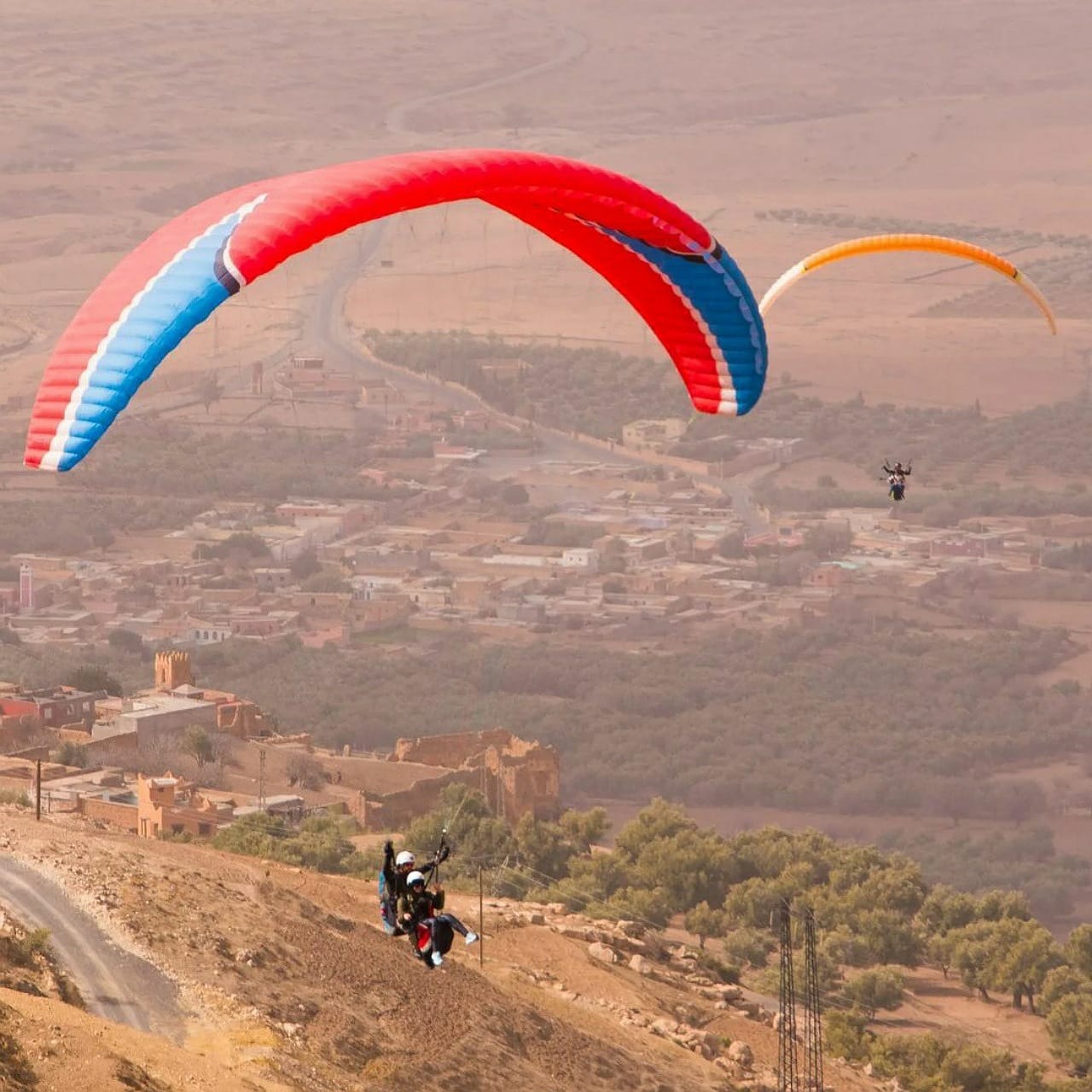 Parapente biplaza volando sobre un pueblo marroquí y olivares cerca de Marrakech