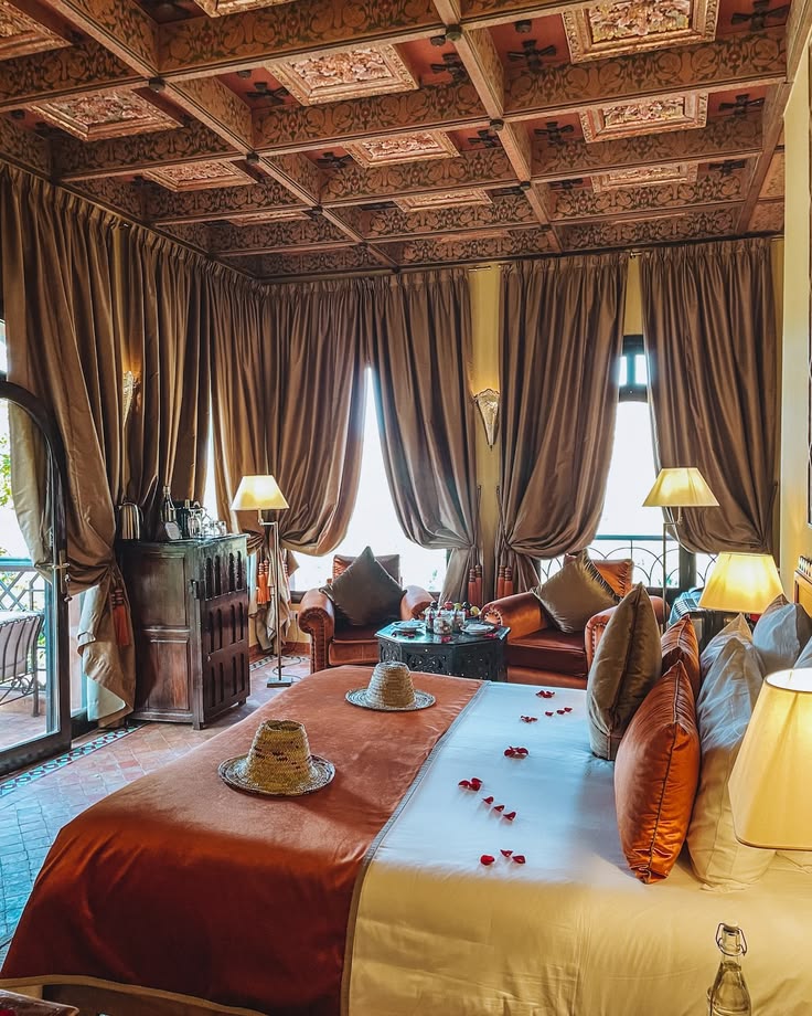 A room at Kasbah Tamadot with a carved painted ceiling, floor-length curtains, a seating area and rose petals laid on the bed