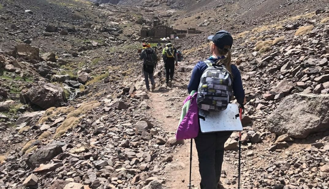 Trekkers walking a rocky trail up the valley towards the Toubkal refuge buildings