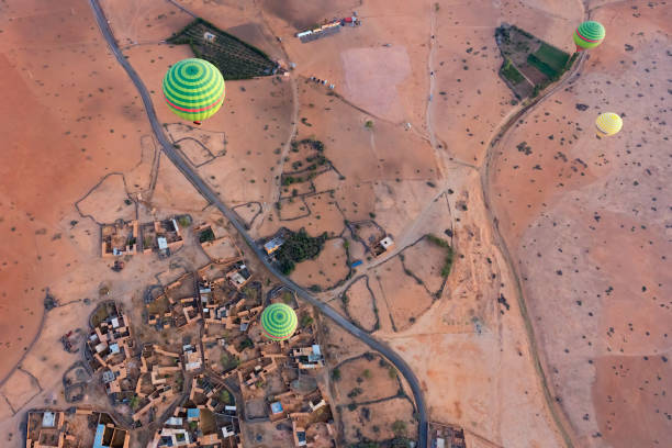 Green and yellow hot-air balloons seen from above, drifting over a village and patchwork fields near Marrakech