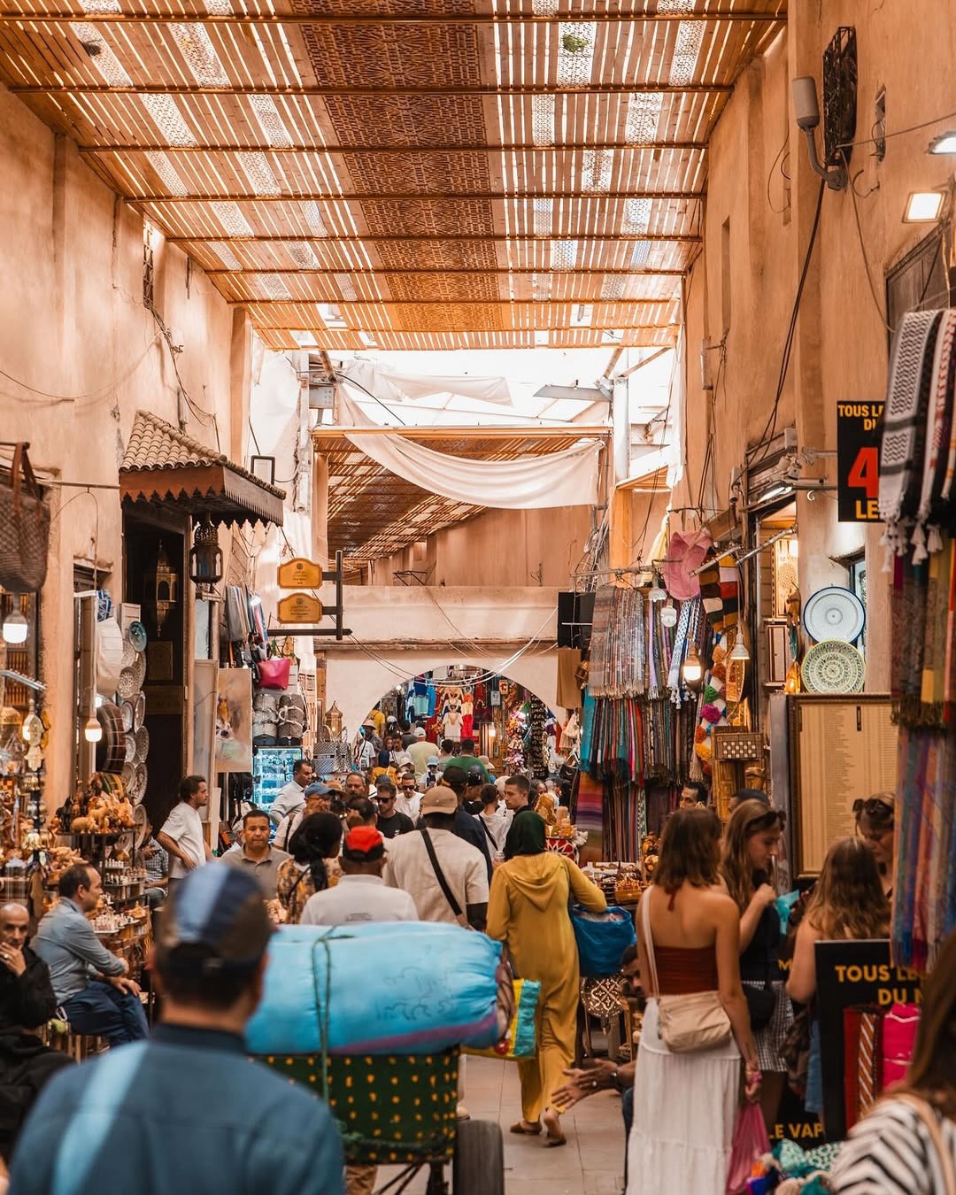 Callejón de un souk de Marrakech con farolillos colgantes, cestas de mimbre y conos de especias de colores
