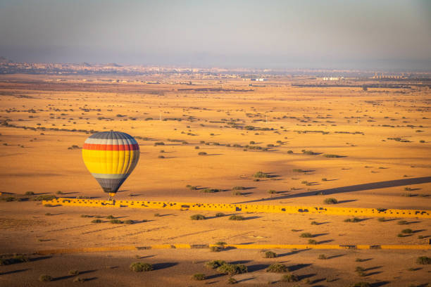 A single striped hot-air balloon drifting low over the golden Marrakech plain at sunrise