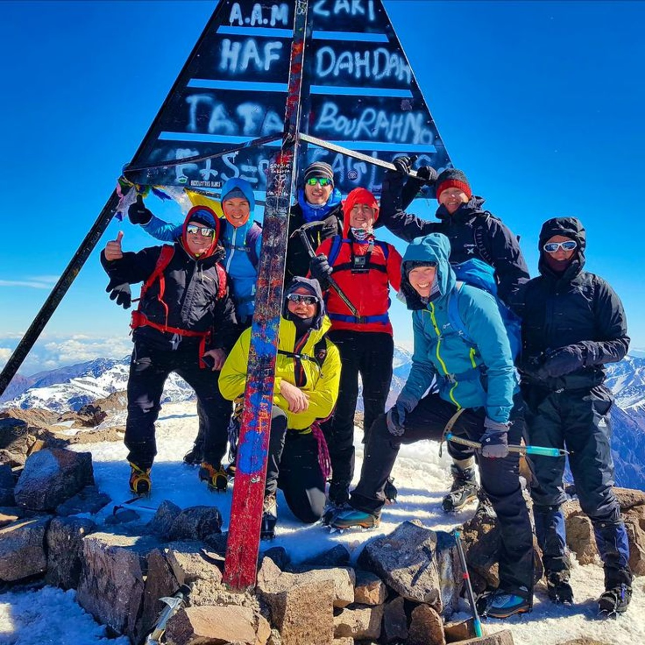 A trekking group celebrating at the Mount Toubkal summit tripod in winter conditions