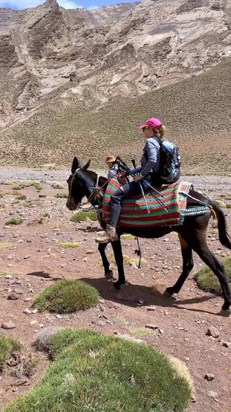 Trekker riding a mule with a colourful woven saddle blanket across a High Atlas valley