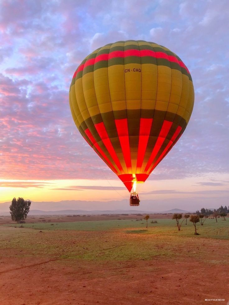 A hot-air balloon burning at low level over a plain at sunrise