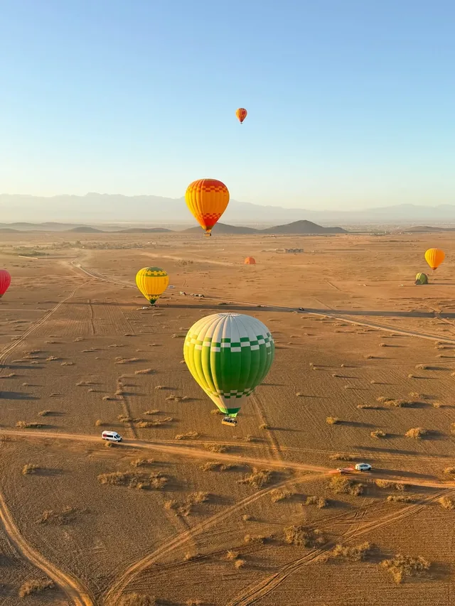 Hot-air balloons drifting over the Marrakech plain with the Atlas mountains behind