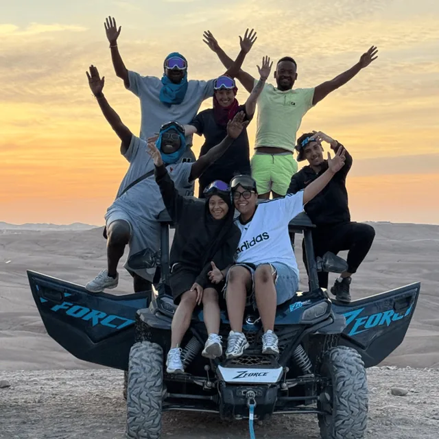 Un gruppo di viaggiatori e guide che festeggiano sopra un buggy al tramonto nel deserto di Agafay