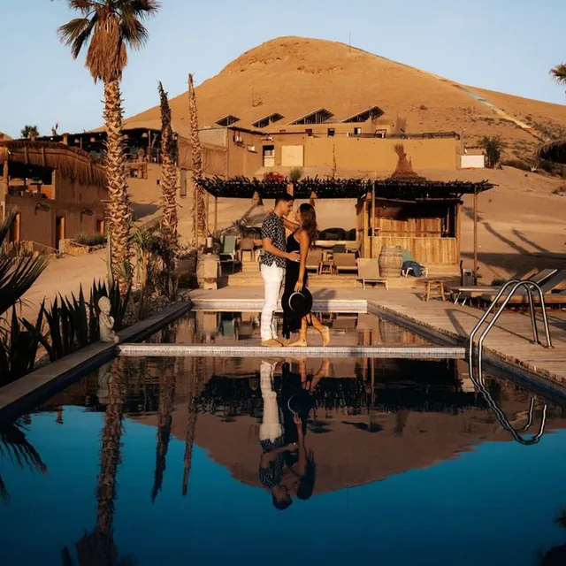 A couple standing beside a desert camp pool at sunset with the reflection of the hill behind them