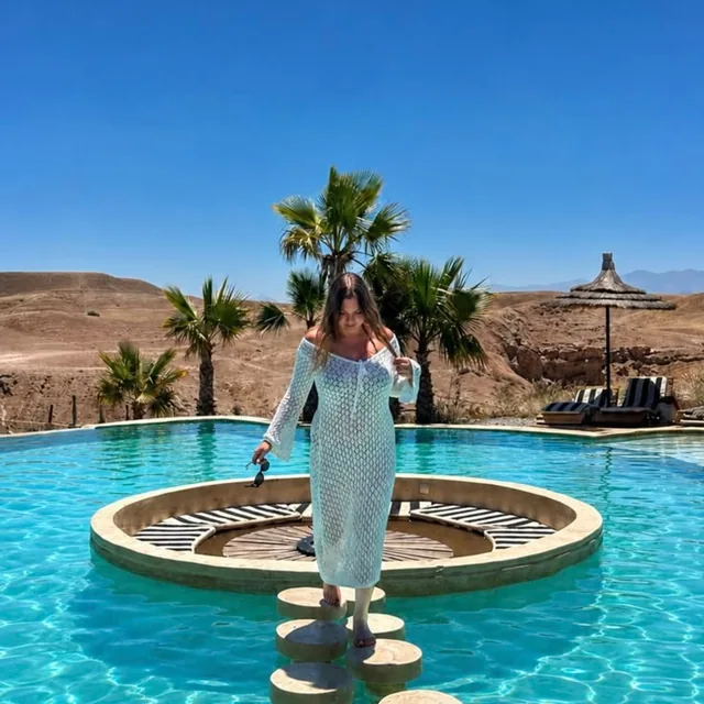 A guest by a desert pool framed by palms with the Agafay hills behind