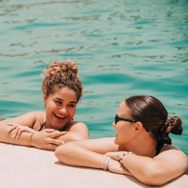 Two friends laughing together at the edge of a turquoise pool