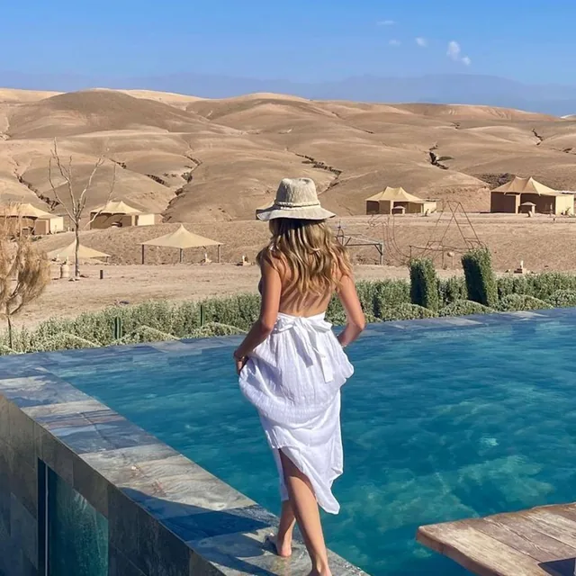 A guest walking along the edge of an infinity pool with desert camp tents and hills behind