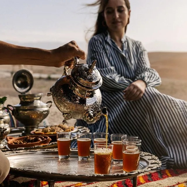 Mint tea poured from a silver pot into glasses on a tray with pastries in the desert