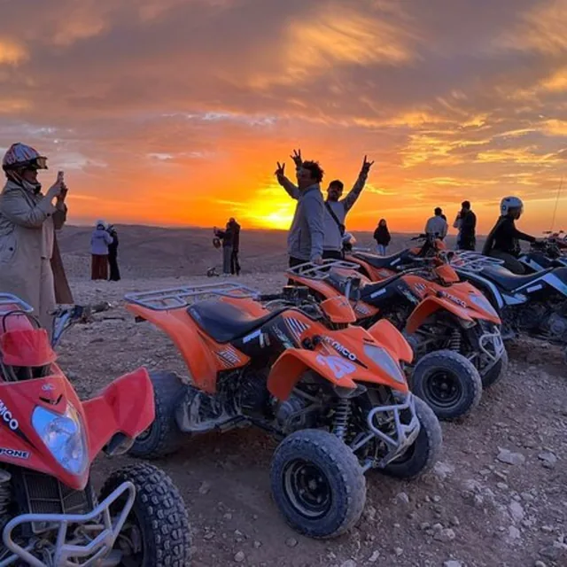 Guests photographing the sunset beside a line of orange quad bikes at a desert viewpoint