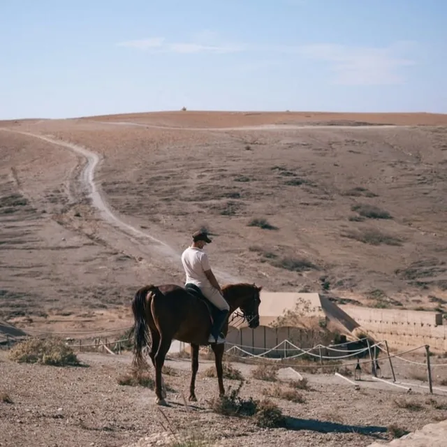 A rider pausing on a ridge above a desert camp in the Agafay