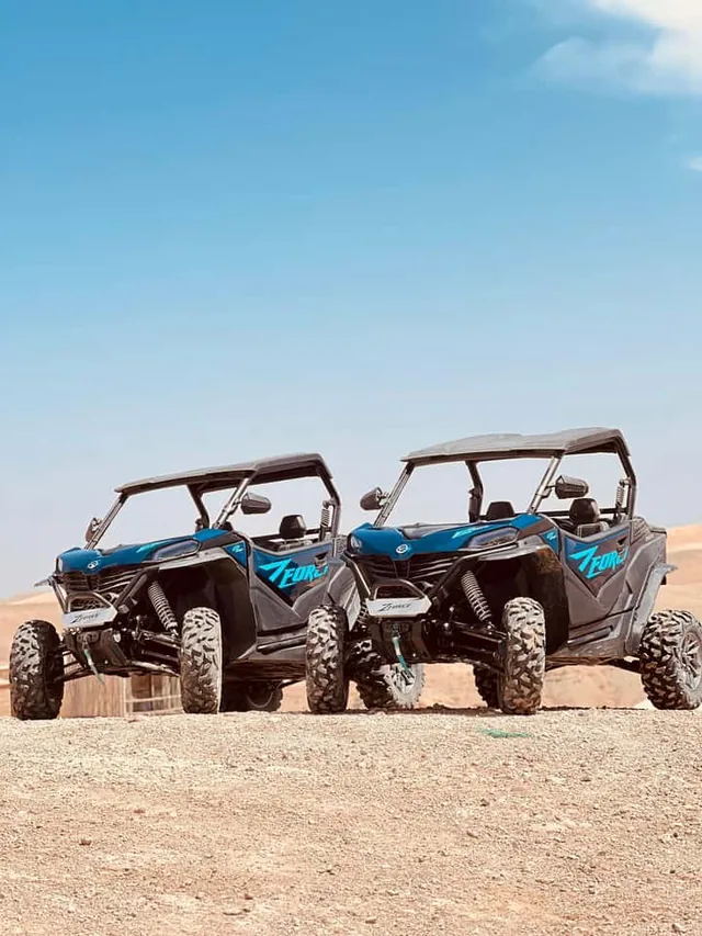 Two blue desert buggies lined up side by side on the Agafay desert plateau under a clear sky