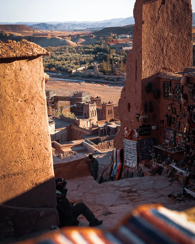 A shaded alley in Aït Ben Haddou lined with craft stalls and opening onto the palm valley