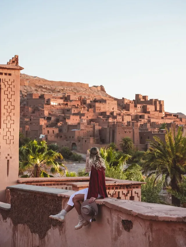 Le ksar de terre d'Aït Ben Haddou vu depuis un mur de terrasse au-dessus de la palmeraie à l'heure dorée