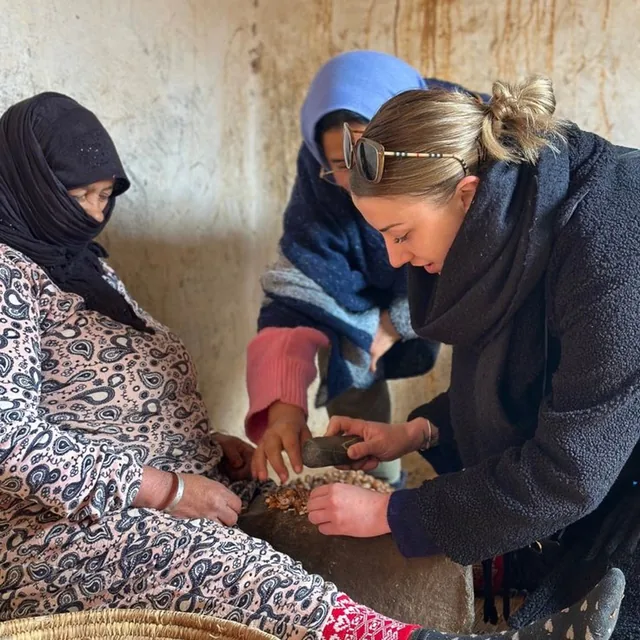 A visitor cracking argan nuts by hand with women at a Moroccan argan cooperative