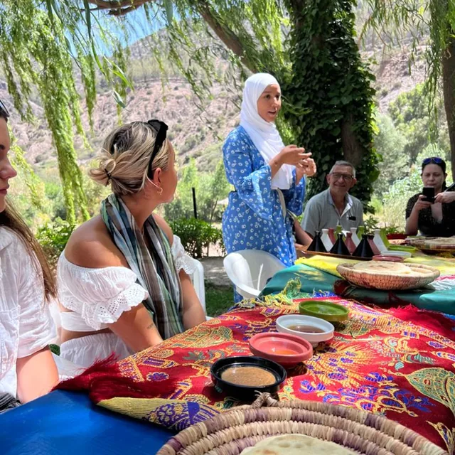 A Berber host explaining local dips and breads to guests at a shaded garden table in the Atlas foothills