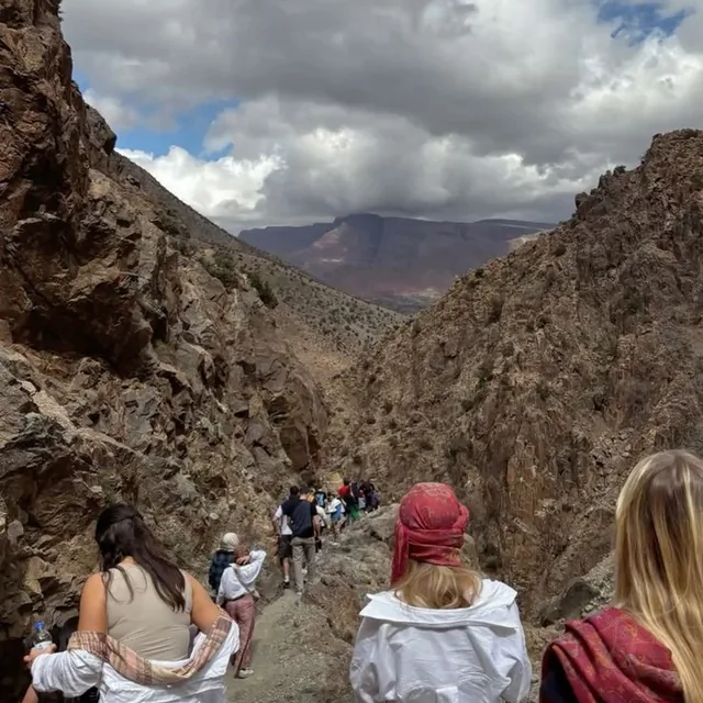 A walking group following a rocky gorge path between steep Atlas cliffs