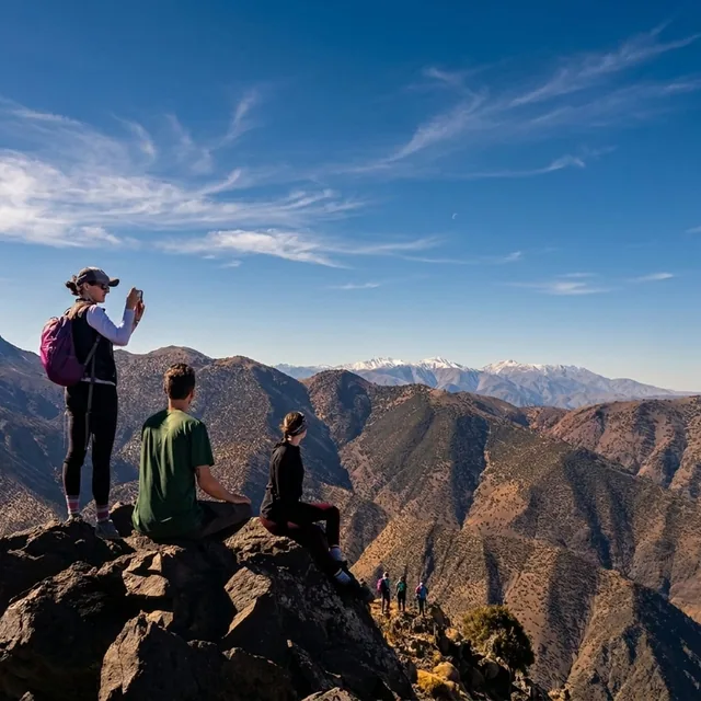 Walkers resting on a rocky Atlas ridge looking out to the snow-capped High Atlas range